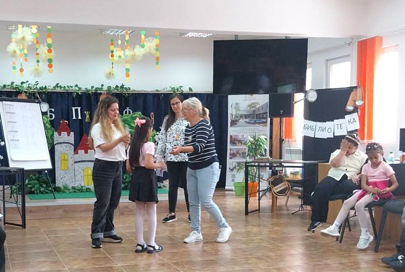 Момиче получава грамота от библиотекари пред декорирана сцена в библиотека.