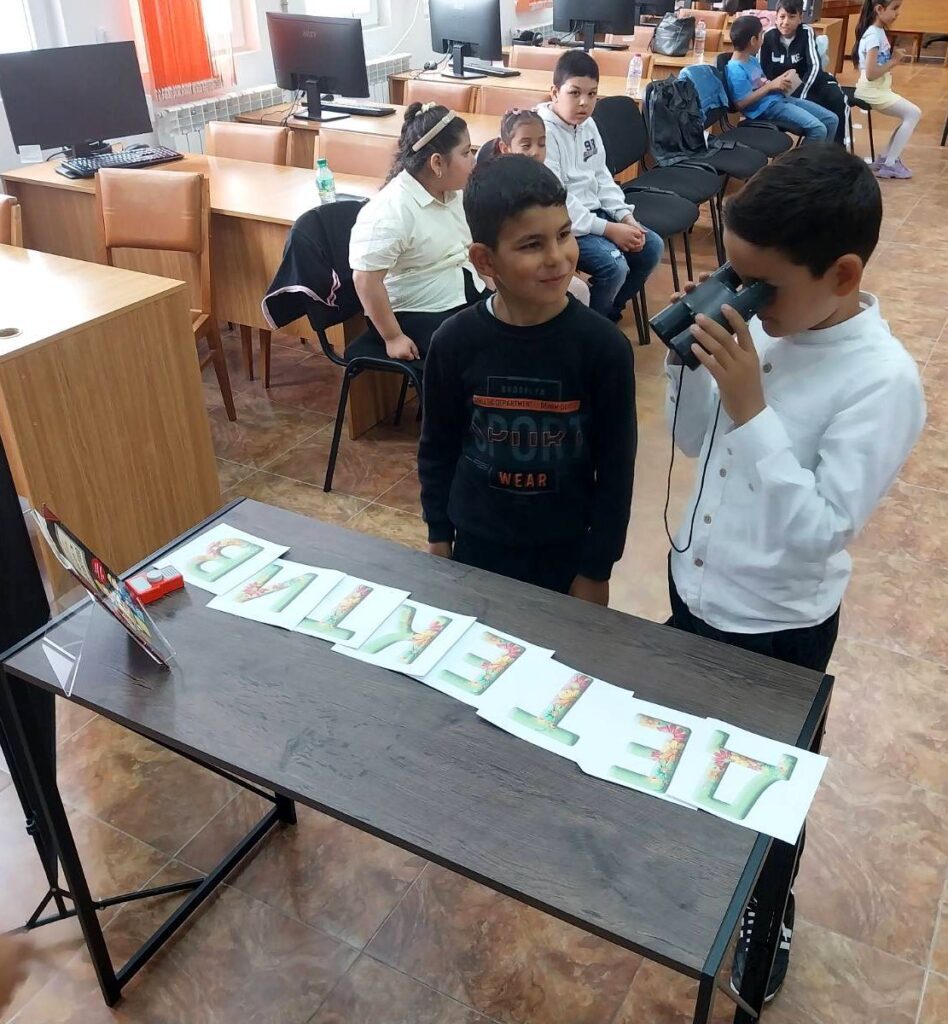 Момче гледа през бинокъл до маса с подредени хартиени букви, изписващи думата „Детектив“.